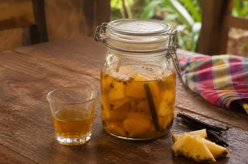 Rhum arrangé ananas et vanille en bocal, avec un verre servi et une gousse de vanille