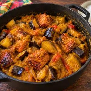 Marmite en fonte de boucané bringelle : morceaux de boucané dorés et cubes d'aubergine avec leur peau, fondus dans une sauce tomate au curcuma, à côté d'un bol de riz blanc