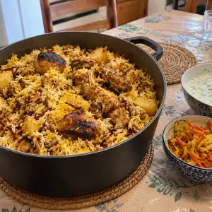 Grande cocotte de briani réunionnais au poulet : riz basmati blanc et jaune safran, morceaux de poulet dorés, pommes de terre et oignons frits, avec un bol de raïta et des achards