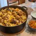 Grande cocotte de briani réunionnais au poulet : riz basmati blanc et jaune safran, morceaux de poulet dorés, pommes de terre et oignons frits, avec un bol de raïta et des achards