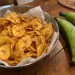 Saladier de chips de banane verte dorées et épicées, à côté de deux bananes plantain vertes