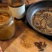 Massalé maison : bocal de poudre brun doré, moulin à café, poêle de graines de coriandre, cumin et moutarde grillées, fenugrec et clous de girofle sur une planche
