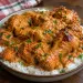 Poulet dakatine servi sur du riz blanc : cuisses et pilons dorés nappés d'une sauce crémeuse à la pâte d'arachide et à la tomate, parsemés d'herbes fraîches