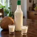 Bouteille de punch coco maison et deux petits verres, à côté d'une noix de coco