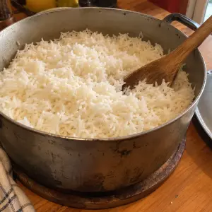 Marmite en fonte un peu usée pleine de riz blanc long grain bien détaché, avec une cuillère en bois, le couvercle posé à côté