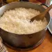 Marmite en fonte un peu usée pleine de riz blanc long grain bien détaché, avec une cuillère en bois, le couvercle posé à côté